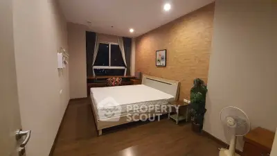 Cozy bedroom with wooden flooring and large window offering night view.