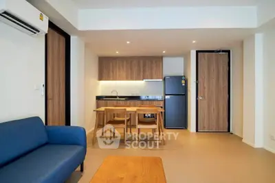 Modern open-plan living room with kitchen and dining area, featuring sleek wooden finishes and cozy seating.