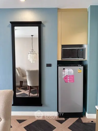 Modern kitchen corner with fridge, microwave, and elegant dining area reflection.