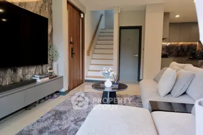 Modern living room with stylish decor and staircase, featuring a large TV and cozy seating area.