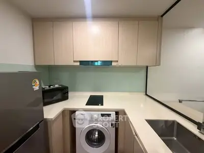 Modern kitchen with washing machine, fridge, and sleek cabinetry in compact layout.