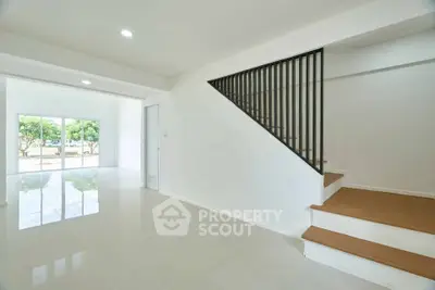 Spacious modern living room with staircase and large windows offering natural light and garden view.