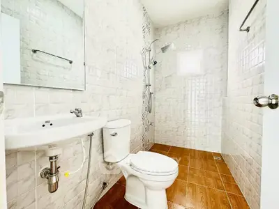 Modern bathroom with white tiles and wooden floor, featuring a shower and sleek fixtures.
