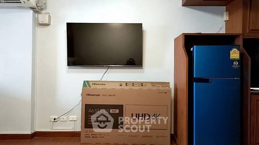 Modern living room with wall-mounted TV and blue refrigerator, showcasing sleek design and functionality.