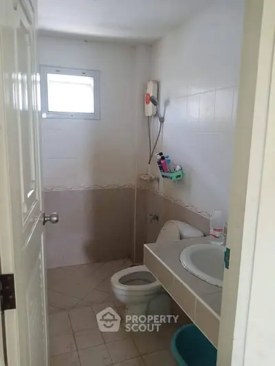Compact bathroom with tiled walls and essential fixtures, featuring a small window for natural light.