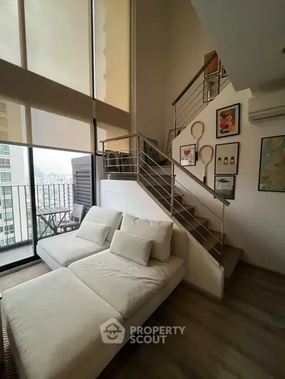 Modern loft with stylish staircase and cozy seating area, featuring large windows and city view.