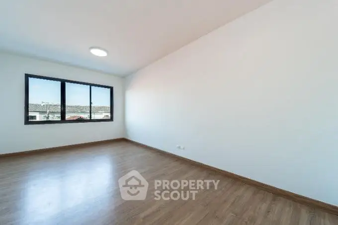Spacious empty room with wooden flooring and large window view.