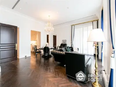 Luxurious spacious living room with elegant dark wood flooring, plush leather sofas, and a sophisticated chandelier, seamlessly connecting to an open layout kitchen.