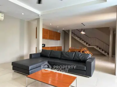 Spacious modern living room with sleek black sofa and open dining area, perfect for entertaining.