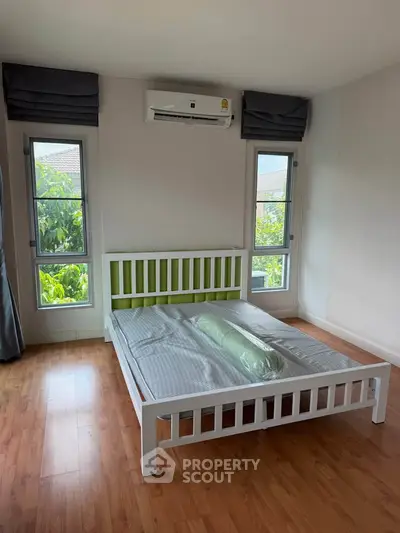 Spacious bedroom with wooden flooring and large windows offering natural light.