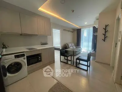 Modern open-layout living room with kitchen, featuring sleek furniture and natural light.