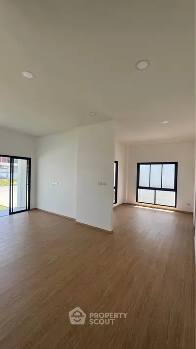 Spacious modern living room with large windows and wooden flooring in a bright, open layout.