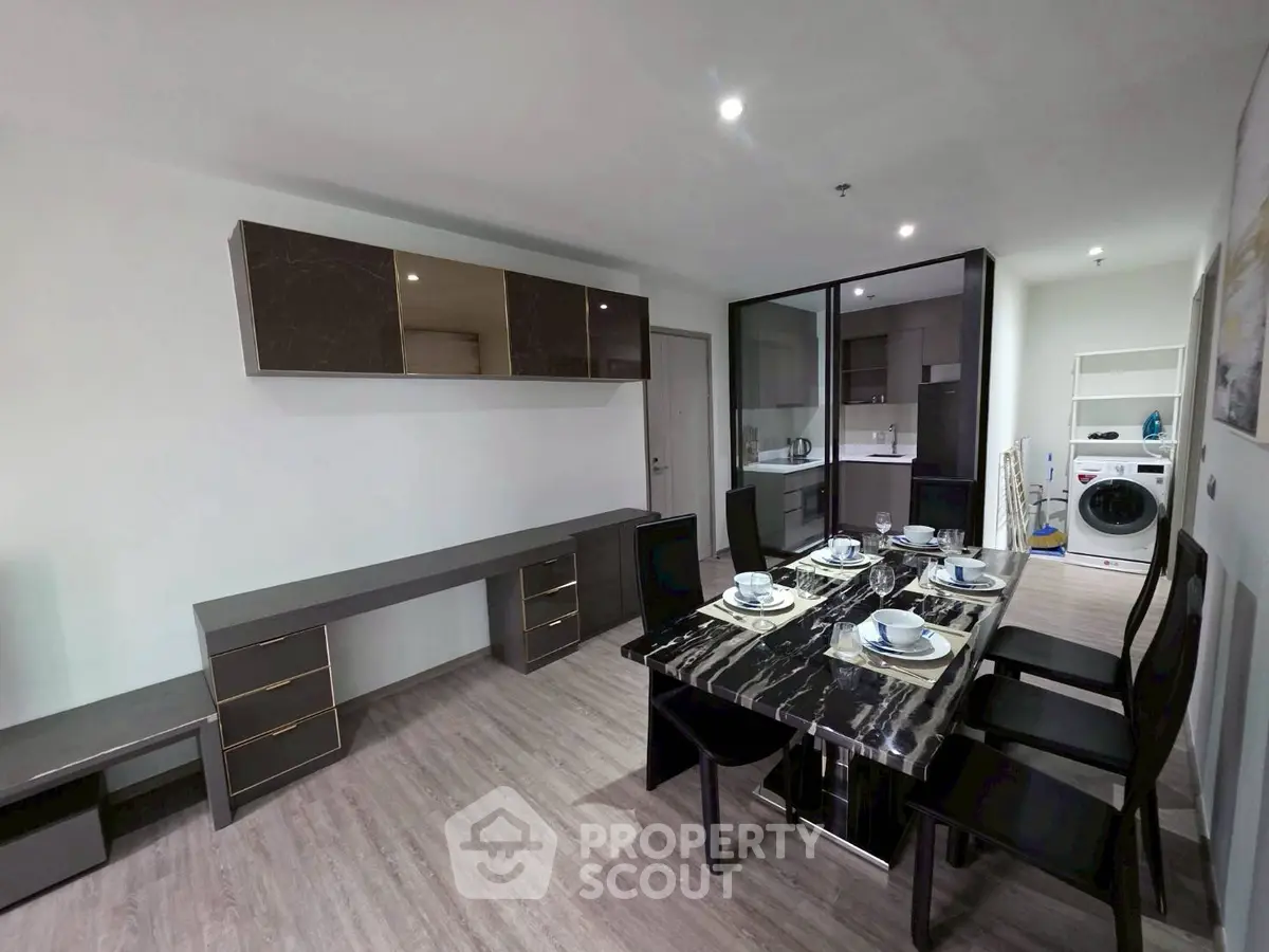 Modern dining area with sleek black table, stylish chairs, and integrated kitchen appliances.