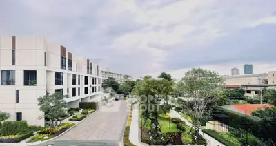 Modern residential building with lush garden and driveway under cloudy sky.