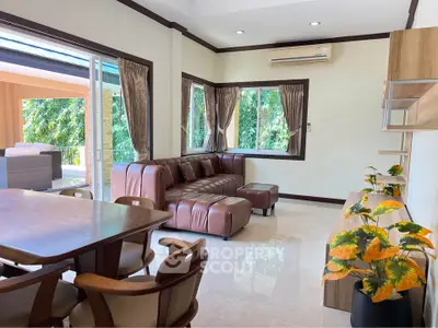 Spacious living room with modern furniture and large windows offering a lush garden view.