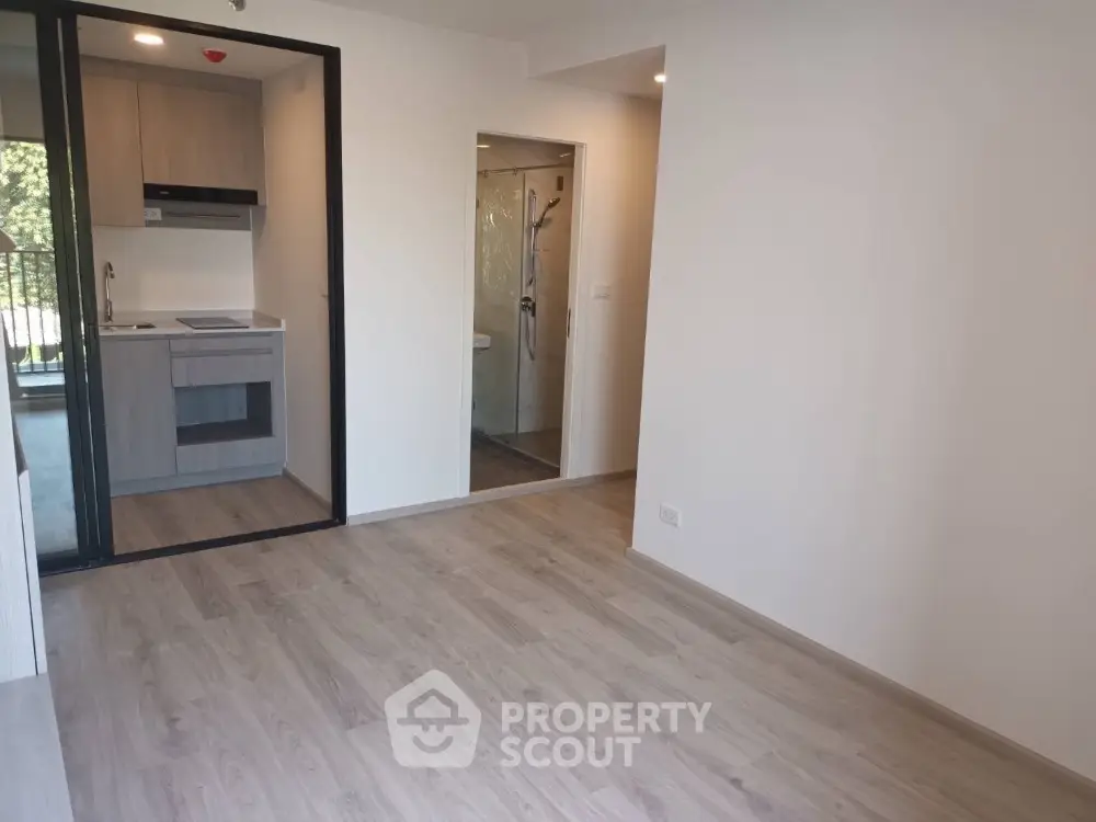 Modern apartment interior with open kitchen and bathroom view, featuring sleek wooden flooring.