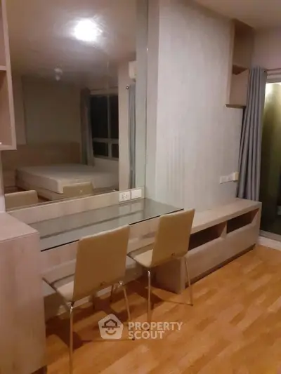 Modern apartment interior with wooden flooring and glass dining table, featuring a cozy bedroom view.