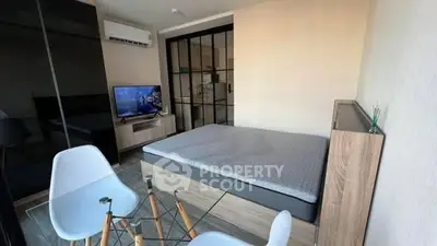 Modern studio apartment with sleek design and glass table, featuring a cozy bed and wall-mounted TV.