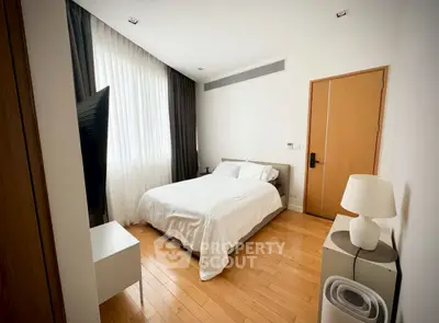 Modern bedroom with sleek design, wooden flooring, and natural light from large window.