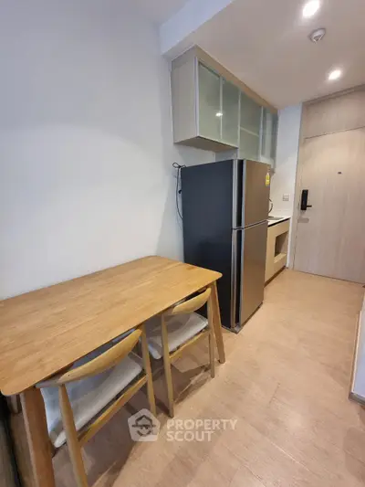 Modern kitchen with sleek fridge and wooden dining set in compact apartment