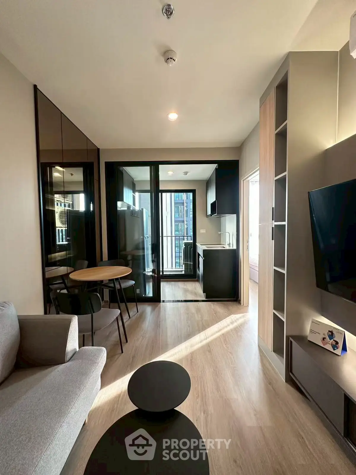 Modern living room with open kitchen and balcony view, featuring sleek furniture and natural light.