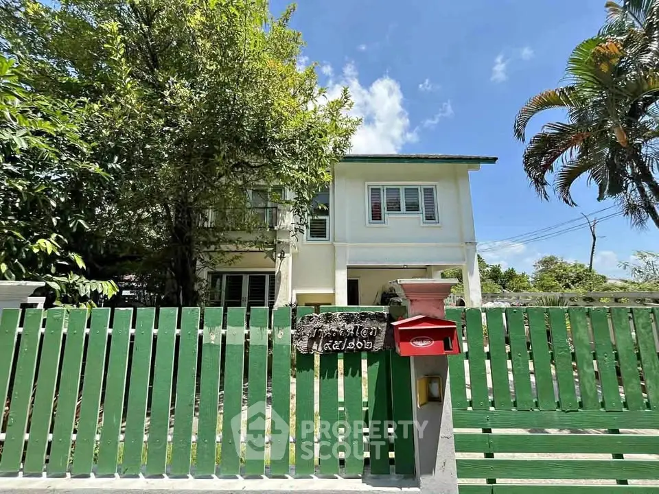 Charming two-story house with green fence and lush garden, perfect for family living.