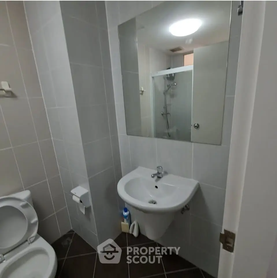 Modern bathroom with sleek fixtures and neutral tiles, featuring a shower and compact sink area.