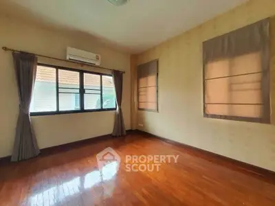 Spacious empty bedroom with wooden floors and large windows in a cozy home.