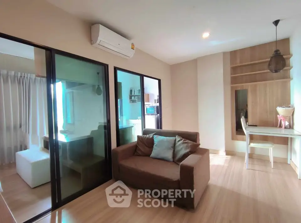 Modern living room with cozy sofa and glass partition leading to kitchen area.