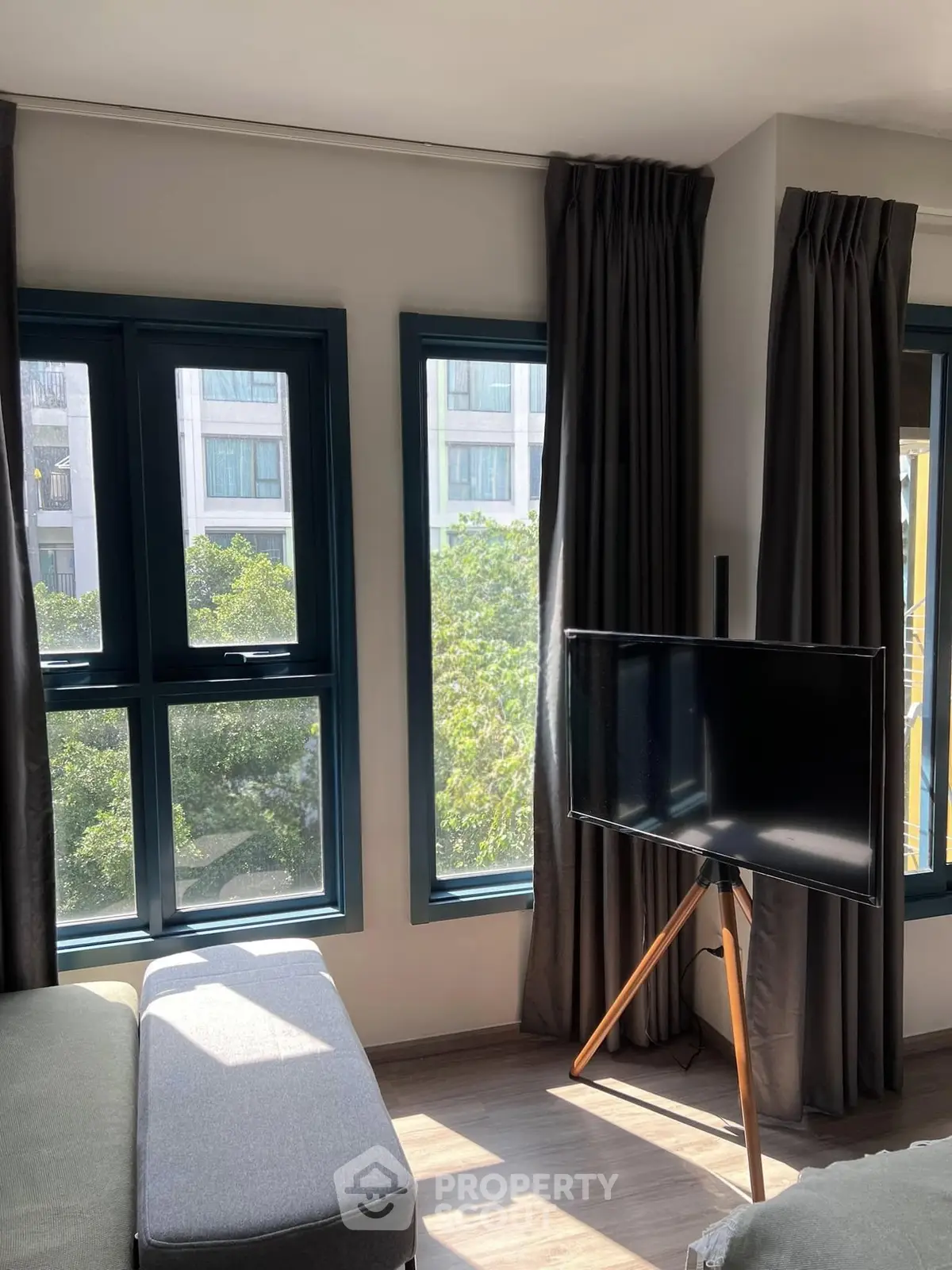 Bright living room with large windows and modern TV stand, offering a serene view of greenery.