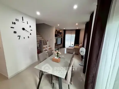 Modern living room with stylish dining area and wall clock, featuring cozy seating and elegant decor.