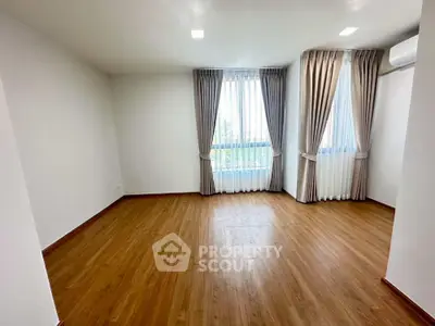 Spacious empty room with wooden flooring and large windows with curtains, perfect for customization.