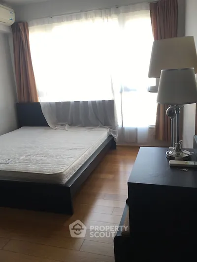 Cozy bedroom with natural light, wooden flooring, and modern furnishings in a stylish apartment.
