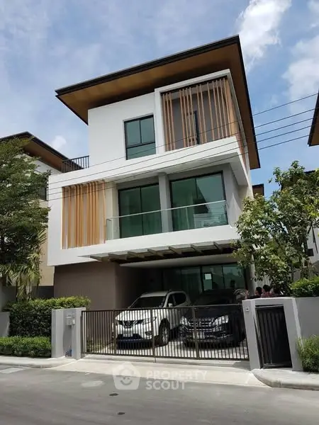 Modern three-story house with sleek design and spacious carport in a suburban neighborhood.