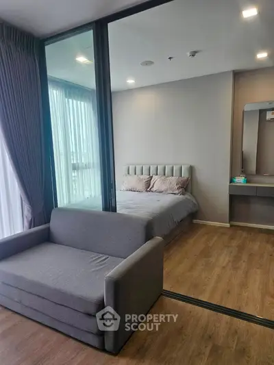 Modern bedroom with glass partition and cozy seating area, featuring stylish decor and natural light.