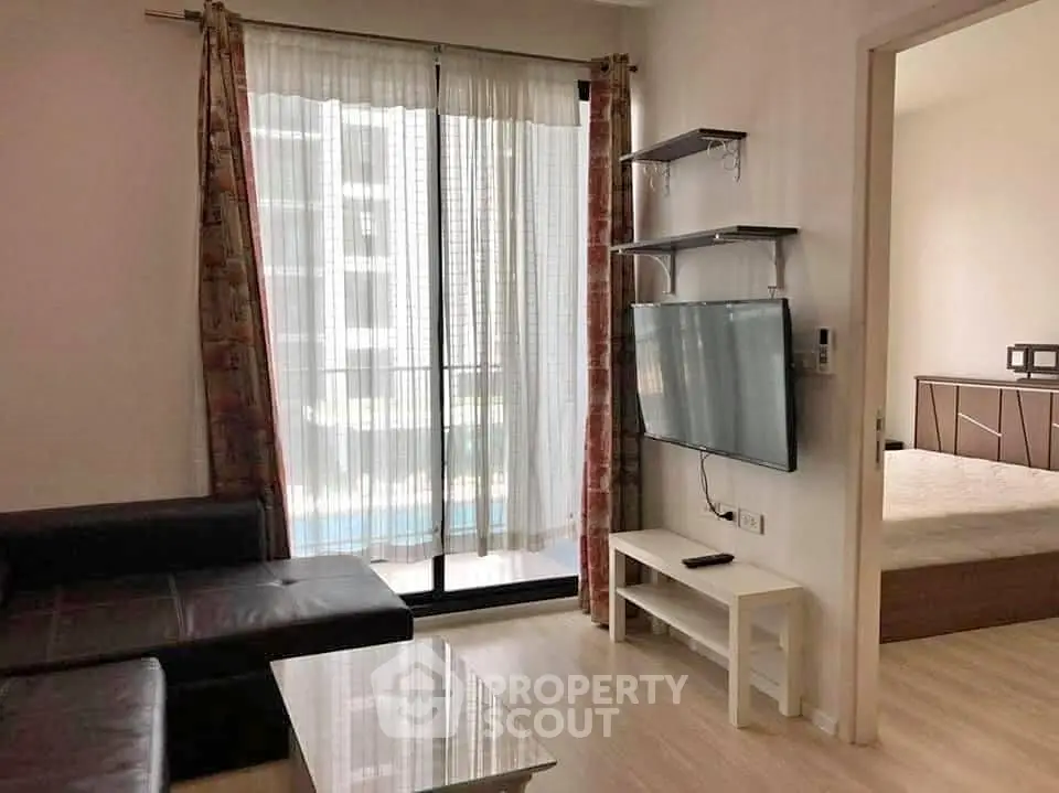 Modern living room with sleek TV and glass coffee table, adjacent to a cozy bedroom, featuring a large window with curtains.