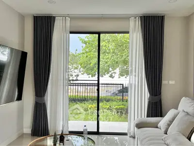 Modern living room with large window and garden view, featuring elegant curtains and comfortable seating.