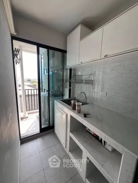 Modern kitchen with sleek white cabinets and balcony access, featuring a compact yet functional design.