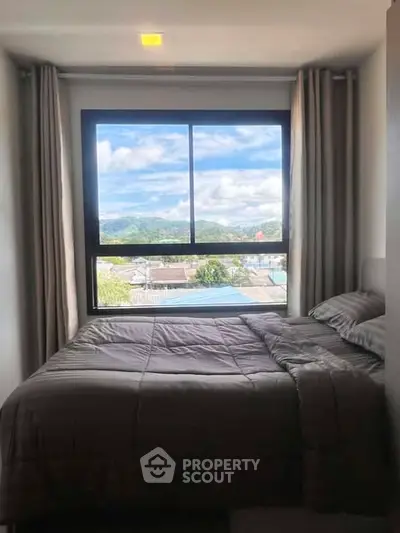 Cozy bedroom with stunning mountain view through large window, perfect for relaxation.