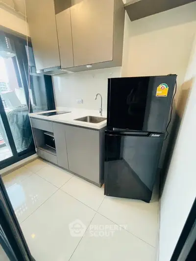 Modern kitchen with sleek cabinetry and black fridge in a compact layout.