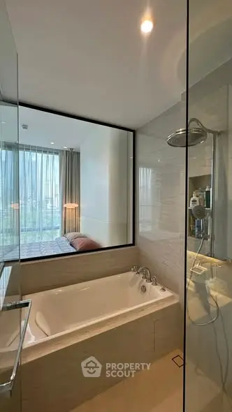 Modern bathroom with bathtub and glass shower, featuring a view into a stylish bedroom.