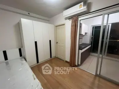 Modern bedroom with sliding glass doors leading to a balcony, featuring sleek wardrobe and air conditioning.