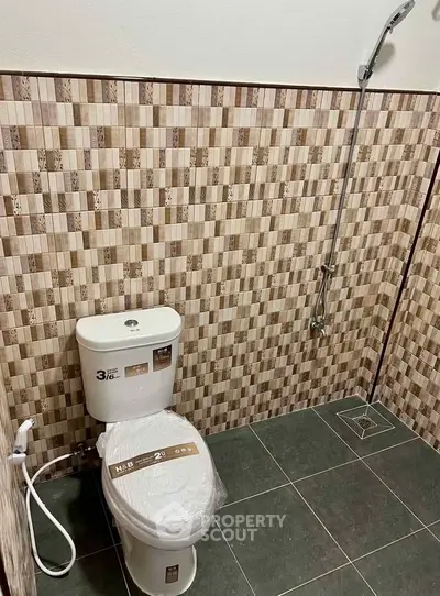 Modern bathroom with tiled walls and floor, featuring a toilet and shower area.