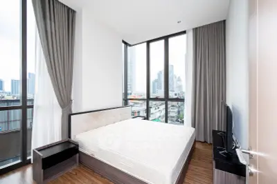 Modern bedroom with large windows offering city views, featuring a sleek design and ample natural light.
