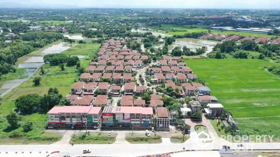 Aerial view of suburban residential development with lush green surroundings and commercial area.