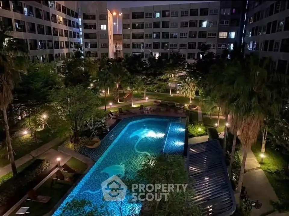 Luxurious apartment complex with illuminated pool and lush gardens at night.
