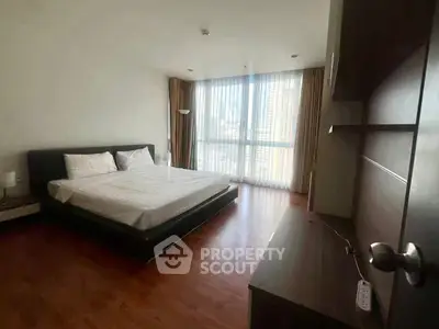 Spacious bedroom with large window and modern furnishings in urban apartment.