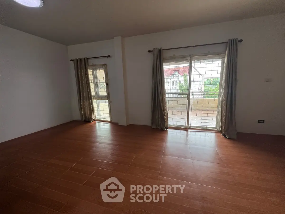 Spacious empty room with wooden flooring and large windows offering natural light.