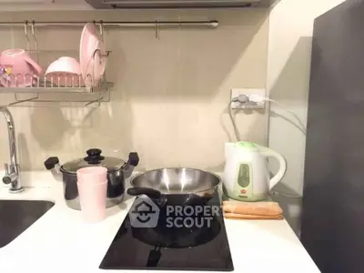 Modern kitchen with electric stove, kettle, and dish rack in compact layout.