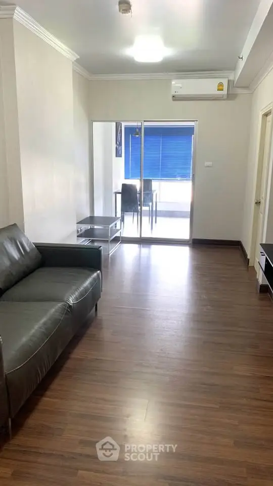 Spacious living room with modern leather sofa and access to balcony, perfect for relaxation.